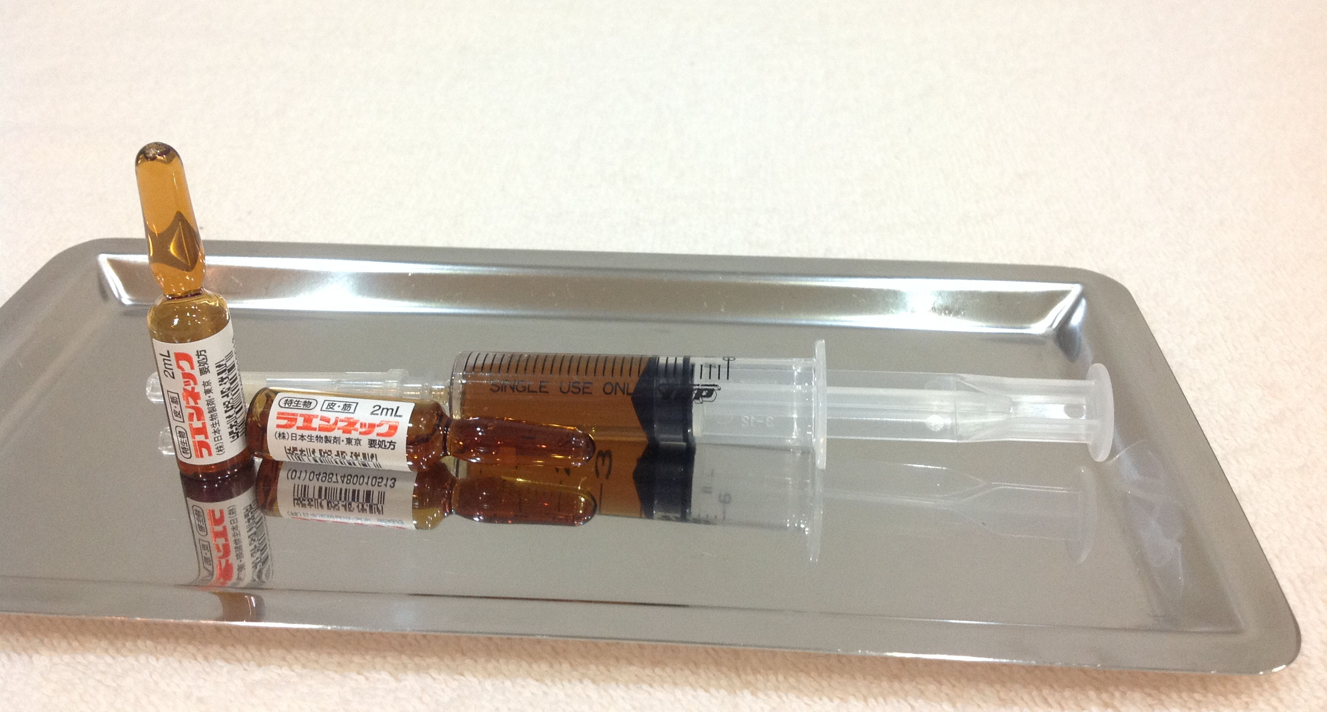 プラセンタ製剤である（株）日本生物のラエンネックのアンプルと注射器の画像です。アンプルは茶褐色で白地のラベルにに赤でラエンネックと書かれてます。注射器は5ccでラエンネック2アンプル4ccの褐色の薬剤で満たされてます。